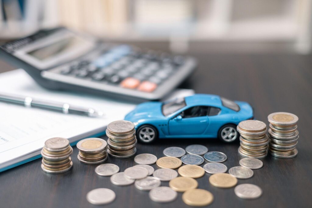Blue toy car on table next to coins, calculator, documents, and a pen to represent auto insurance policies
